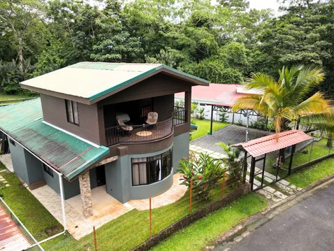 Two-story modern home with covered balcony, tropical landscaping, and gated driveway in La Fortuna, Costa Rica.
