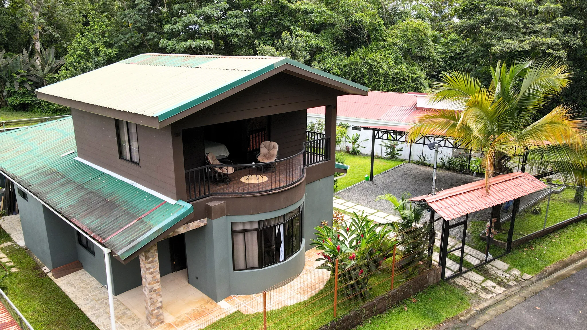 Two-story modern home with covered balcony, tropical landscaping, and gated driveway in La Fortuna, Costa Rica.